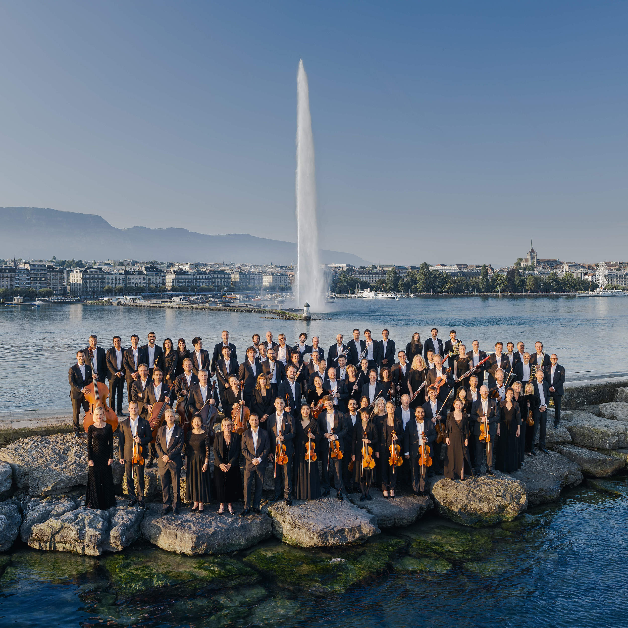 Photo of the Orchestre de la Suisse Romande posing in front of the Geneva Jet d'Eau, a landmark in Switzerland that combines the elegance of classical music with the beauty of the Geneva landscape