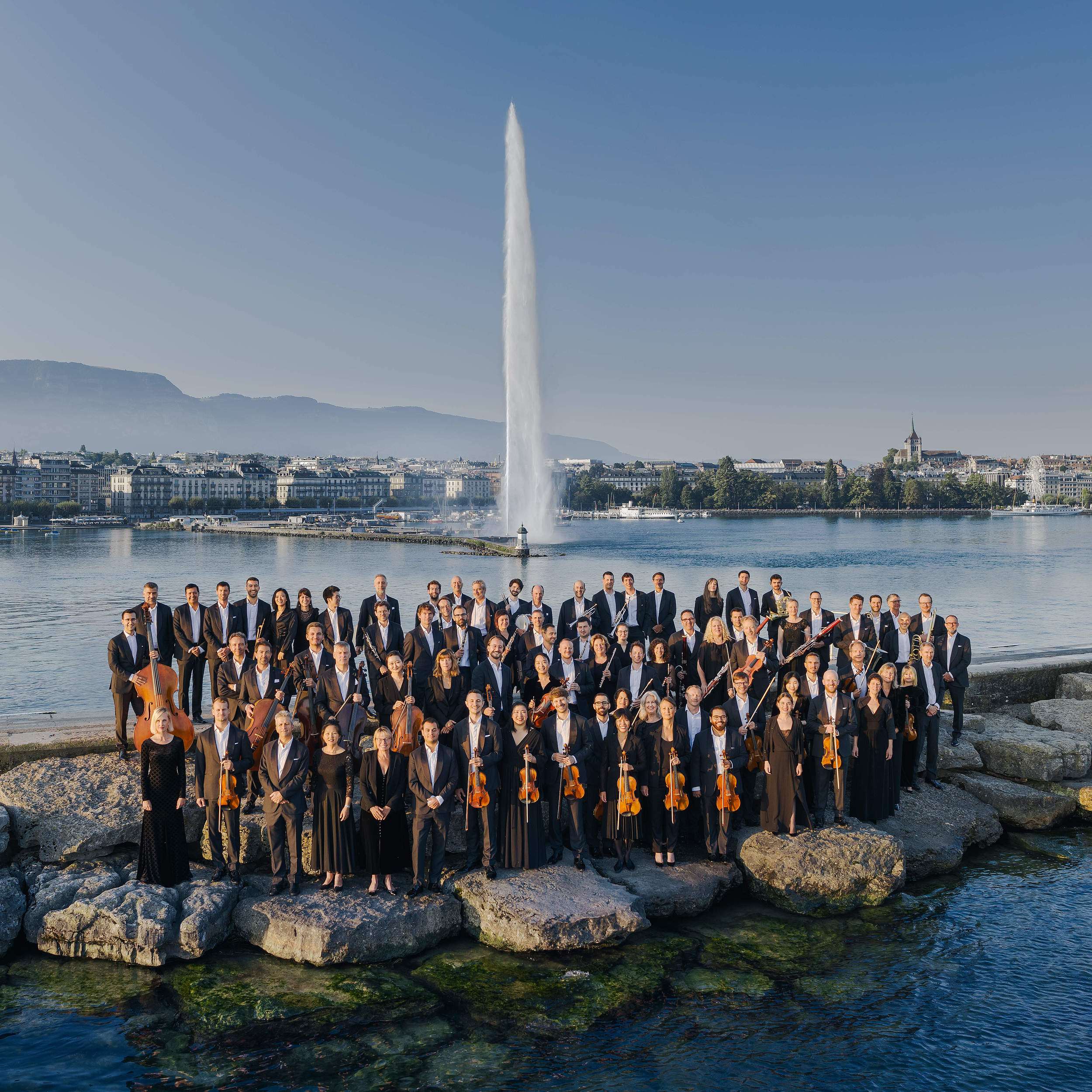 Photo of the Orchestre de la Suisse Romande posing in front of the Geneva Jet d'Eau, a landmark in Switzerland that combines the elegance of classical music with the beauty of the Geneva landscape
